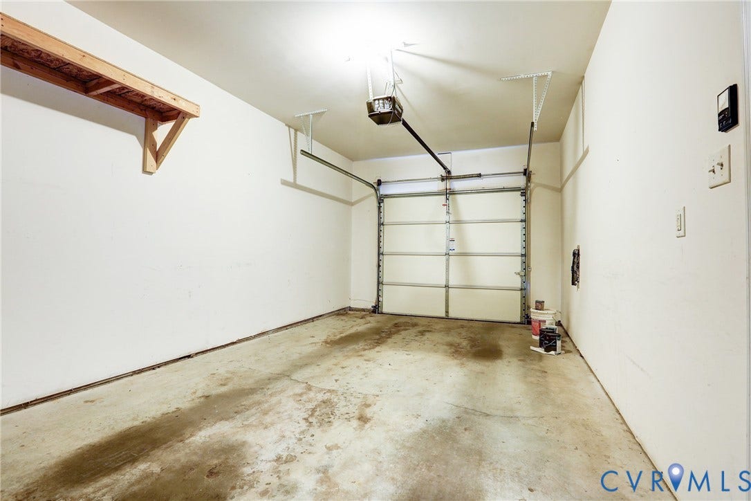 Single-car garage featuring a sectional overhead door, automatic door opener, concrete flooring, and built-in wall-mounted wooden shelving