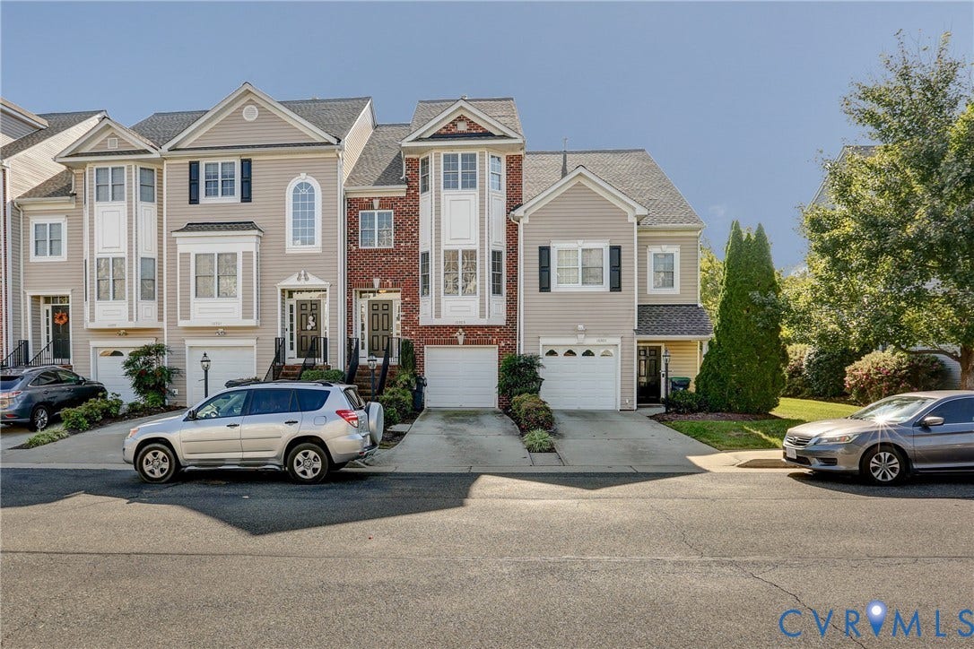 Multi-story townhouse exterior featuring vinyl siding, brick accents, multi-pane windows, and integrated garage doors
