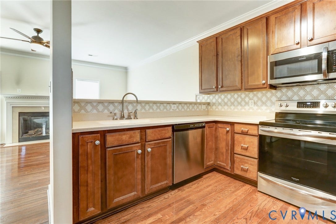 Kitchen featuring wood cabinetry, stainless steel appliances, patterned tile backsplash, and wood-finish flooring