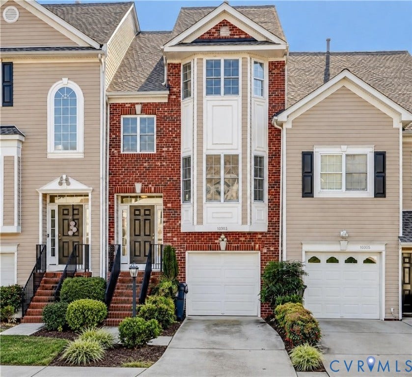 Multi-level facade featuring red brick masonry and horizontal siding, a central bay window, arched window detailing, and individual concrete driveways with attached garage bays