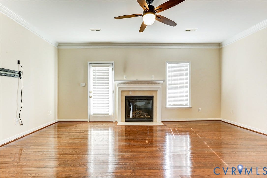 Wood-finish flooring, fireplace with a decorative mantel, crown molding, ceiling fan with integrated lighting, and a glass-paneled exterior door