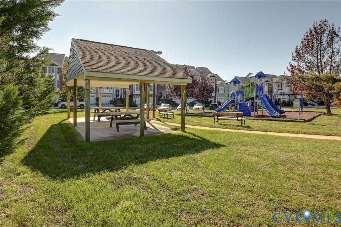 Community common area featuring a covered pavilion, playground equipment, manicured lawn, and paved walkways