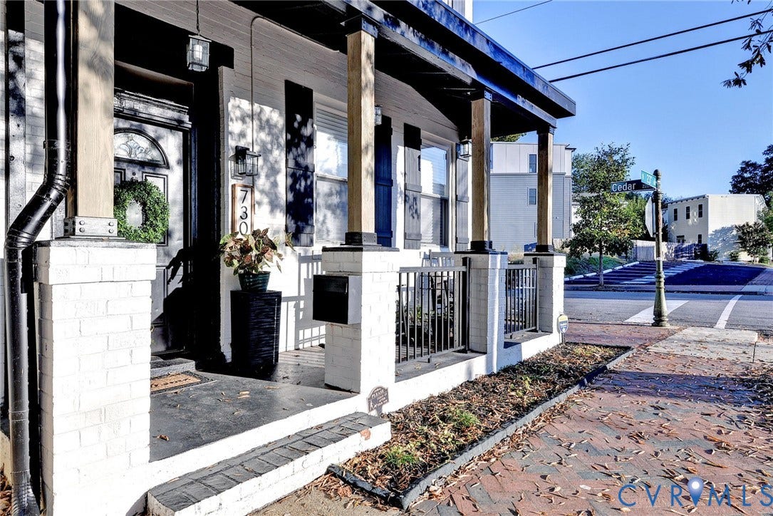 730 N 23RD Street, Union Hill, Richmond, VA 23223 Covered front porch featuring white brick pillars, wood-finish support columns, a black metal railing, and a dark-toned entryway with arched transom window
