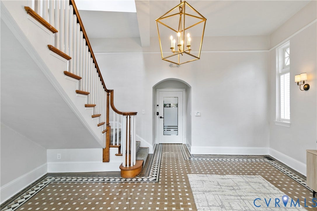 2800 Patterson Avenue, Richmond, VA 23221 Entryway featuring a geometric metal pendant light, a staircase with a natural wood-finish handrail and painted balusters, patterned tile flooring, an arched doorway, and wall-mounted sconce lighting