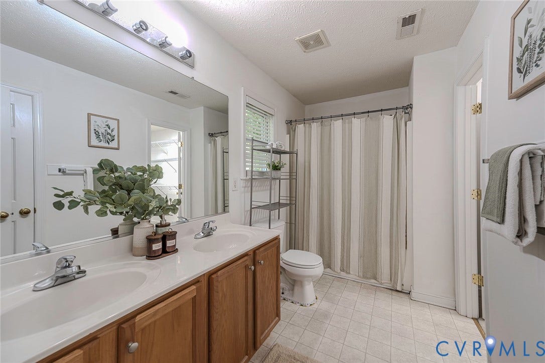 2408 Swartwout Avenue, Woodland Hills, Henrico, VA 23228 Dual-sink vanity with a solid-surface countertop, full-width vanity mirror, four-light vanity fixture, and a shower-tub combination with a sliding rod