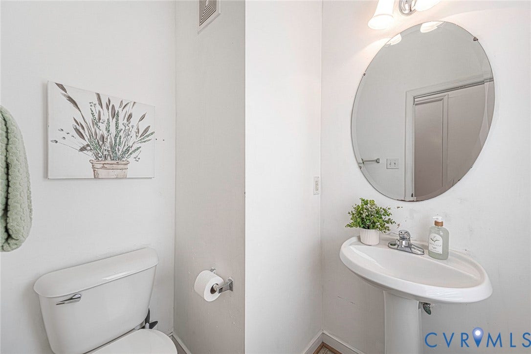 2408 Swartwout Avenue, Woodland Hills, Henrico, VA 23228 Pedestal sink with a single-handle faucet, circular wall-mounted mirror, and wall-mounted light fixture
