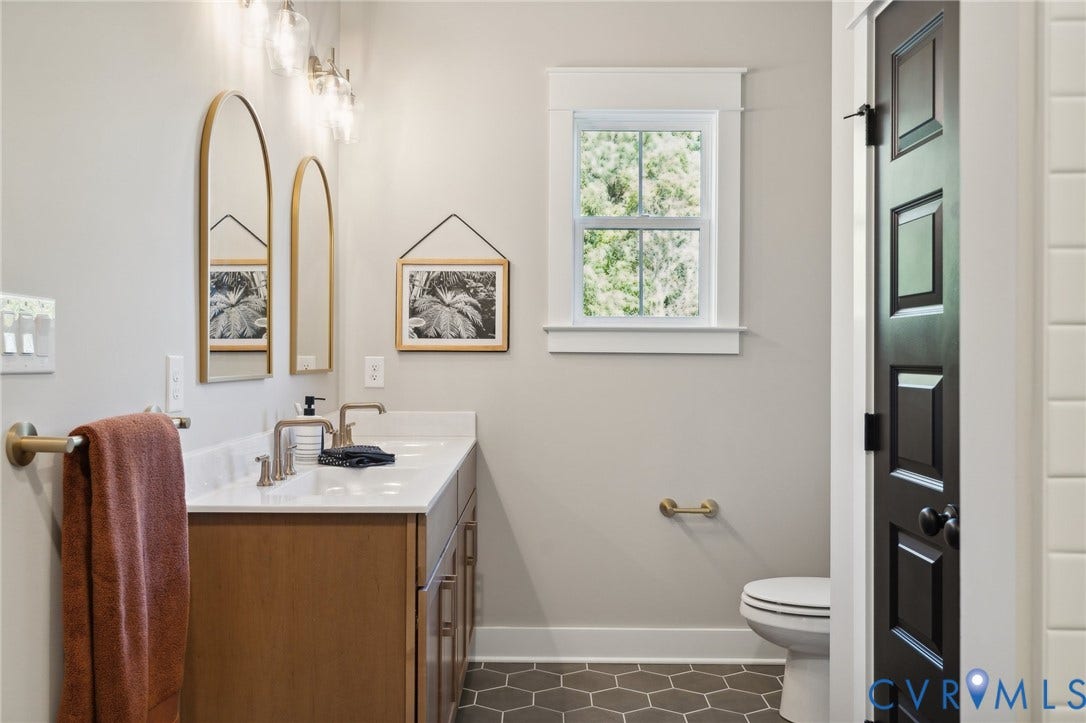 18128 Dogwood Trail Way, Rockville, VA 23146 Dual-sink vanity with light wood cabinetry, quartz countertop, arched wall-mounted mirrors, brass hardware, and hexagonal tile flooring