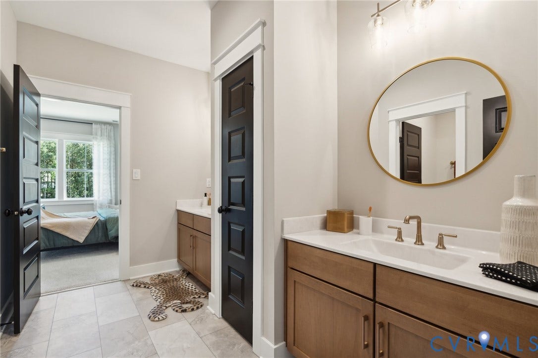 18128 Dogwood Trail Way, Rockville, VA 23146 Bathroom featuring wood-finish cabinetry with white countertops, oval mirror with gold-toned frame, multi-light vanity fixture, and neutral tile flooring