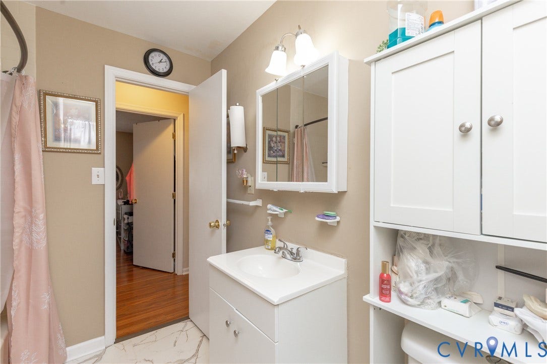 2108 Ridgemont Road, Richmond, VA 23224 Bathroom featuring a white vanity cabinet with a drop-in sink, a wall-mounted medicine cabinet with integrated lighting, built-in white cabinetry, and stone-finish tile flooring