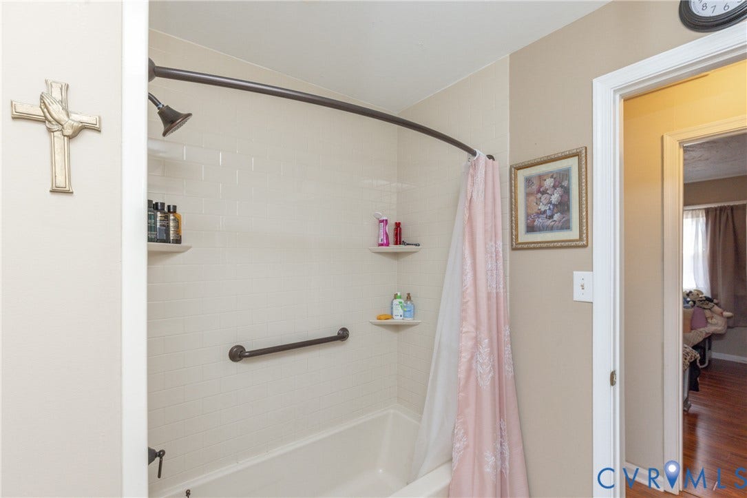 2108 Ridgemont Road, Richmond, VA 23224 Shower enclosure featuring white subway tile surround, built-in shelving, a curved shower rod, and a wall-mounted safety grab bar