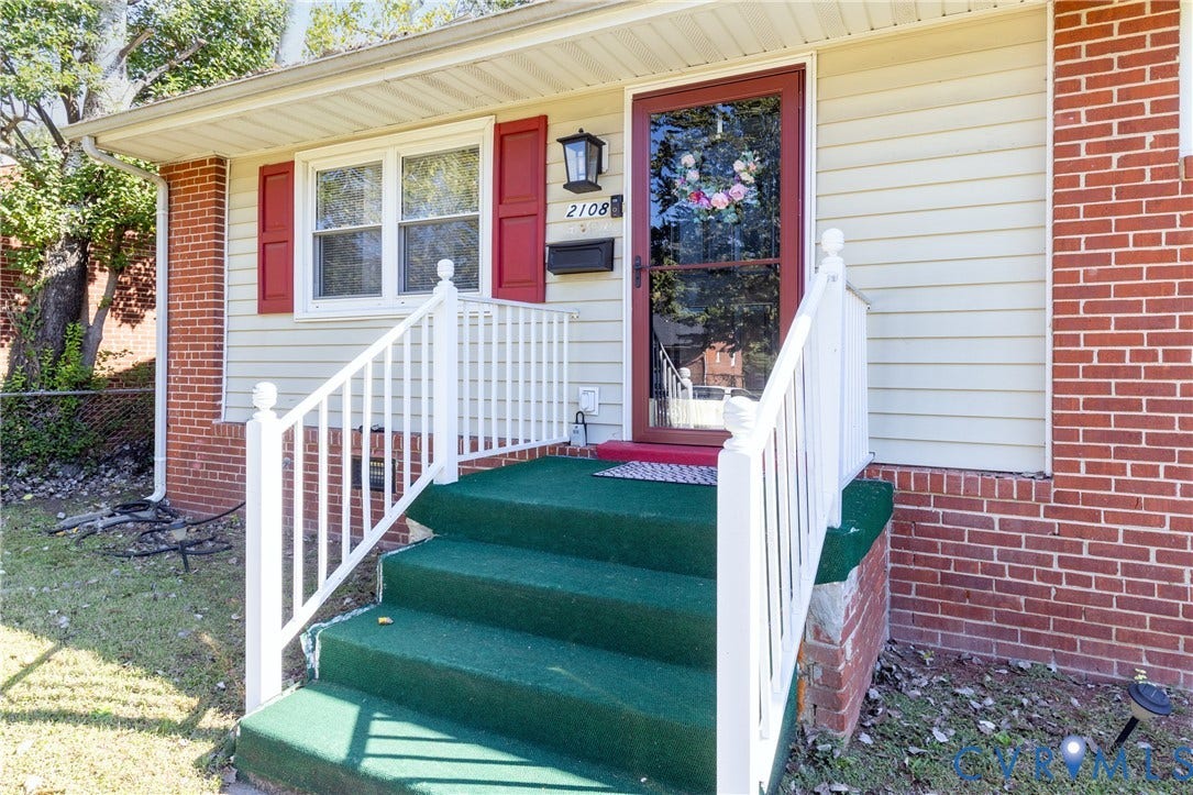 2108 Ridgemont Road, Richmond, VA 23224 Exterior featuring red brick masonry corners, light-toned horizontal siding, contrasting red window shutters, and white railings