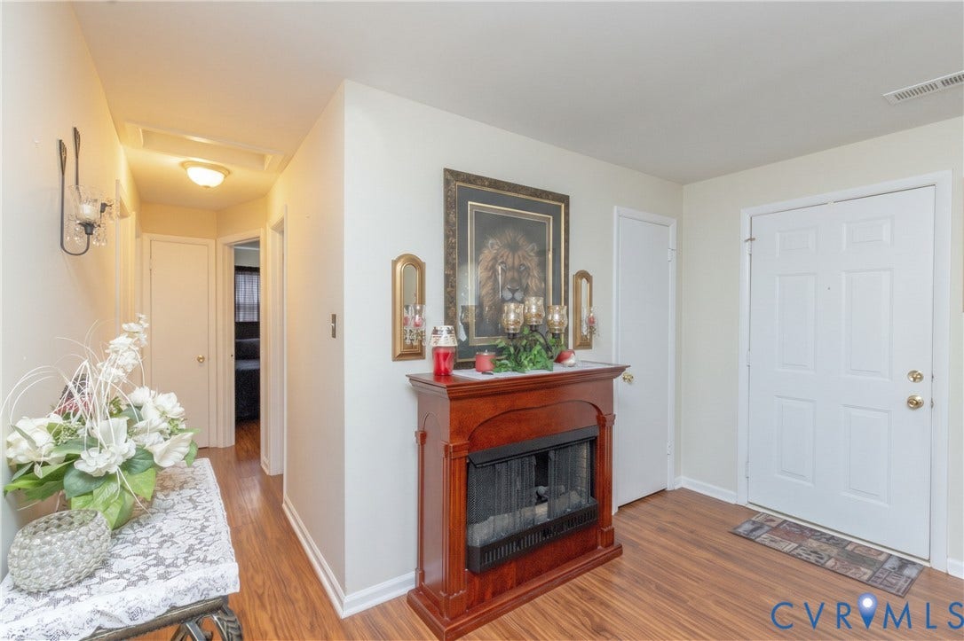 2108 Ridgemont Road, Richmond, VA 23224 Interior entryway featuring wood-finish flooring, a wood-finish fireplace mantel with a metal screen, wall-mounted sconce lighting, and a paneled entry door