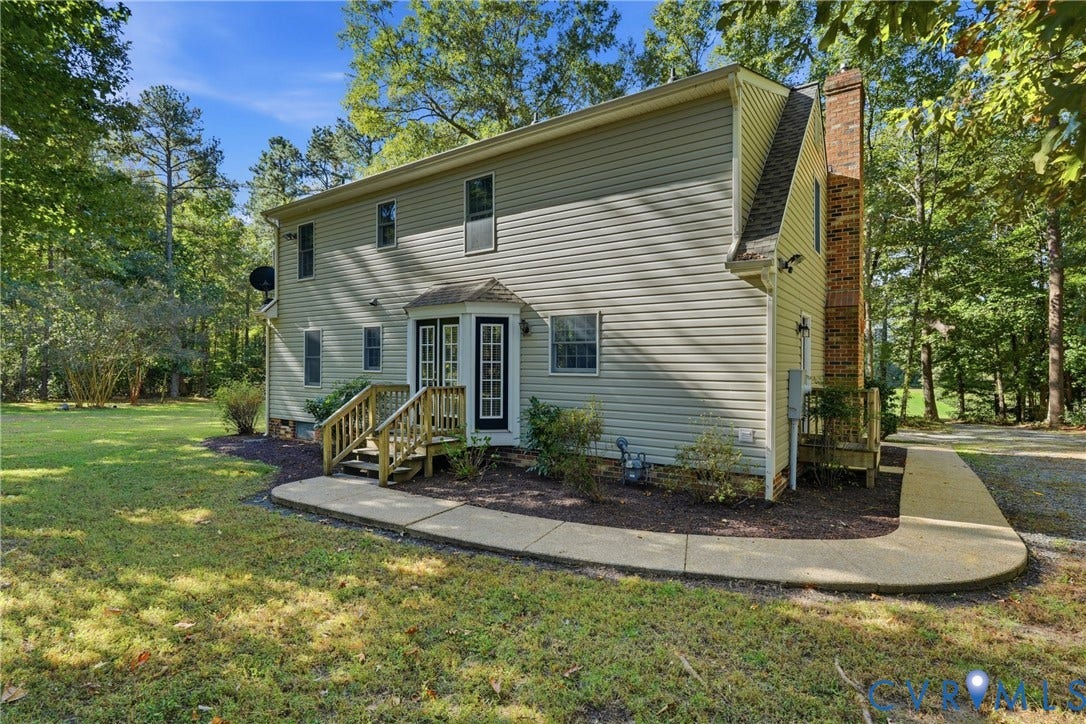 7270 Crossing Oaks Trail, Mechanicsville, VA 23111 Two-story exterior featuring light-colored horizontal siding, a prominent brick chimney, multi-pane glass entry doors, wooden steps, and a curved concrete walkway