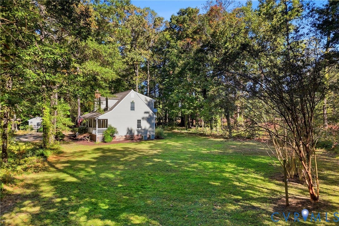 7270 Crossing Oaks Trail, Mechanicsville, VA 23111 Expansive backyard featuring a level lawn, mature trees, and a residential structure with a covered porch and brick foundation