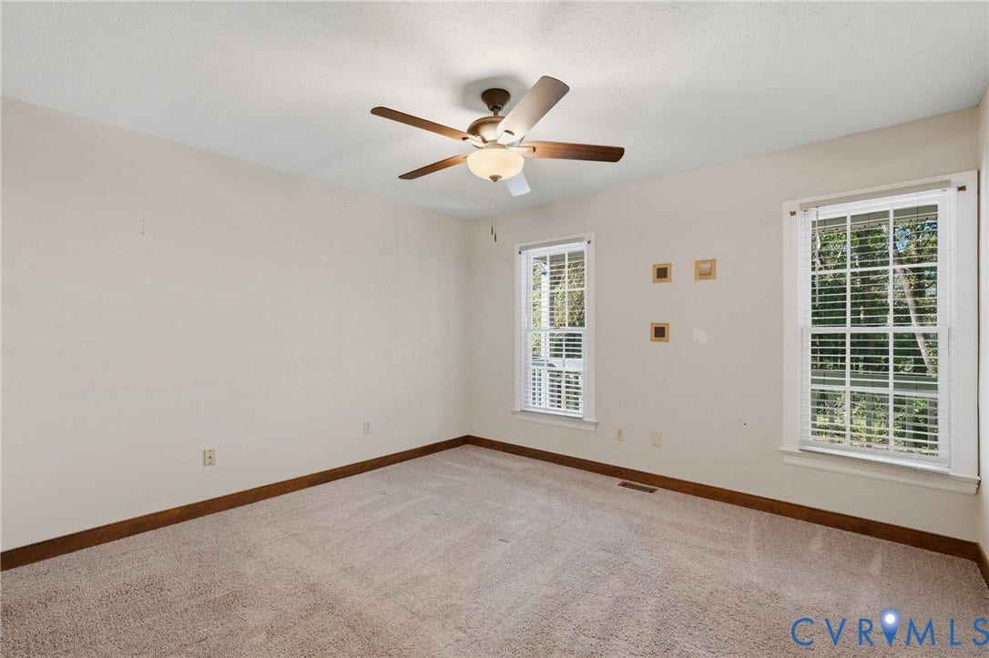 7270 Crossing Oaks Trail, Mechanicsville, VA 23111 Neutral-toned interior space featuring wall-to-wall carpeting, wood-finish trim, dual double-hung windows, and a central ceiling fan with integrated lighting