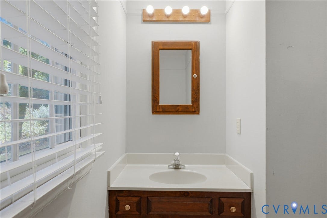 7270 Crossing Oaks Trail, Mechanicsville, VA 23111 Bathroom featuring a wood-finish vanity with a built-in basin, coordinating wall-mounted medicine cabinet, four-light vanity fixture, and horizontal window blinds