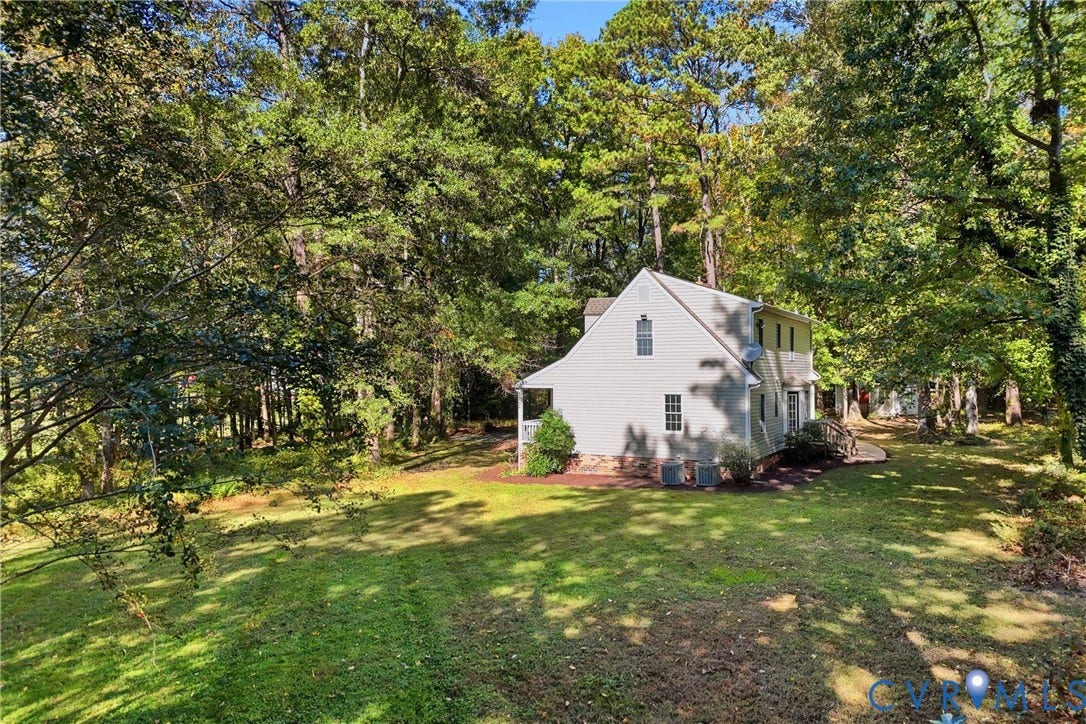 7270 Crossing Oaks Trail, Mechanicsville, VA 23111 Two-story residence with light-colored siding, brick foundation detail, expansive lawn, and mature canopy trees