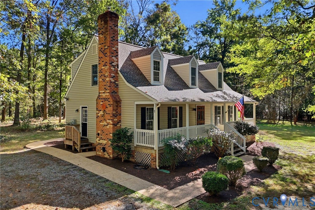 7270 Crossing Oaks Trail, Mechanicsville, VA 23111 Two-story residence featuring light-toned horizontal siding, a prominent brick chimney, multiple dormer windows, and a covered front porch with railings