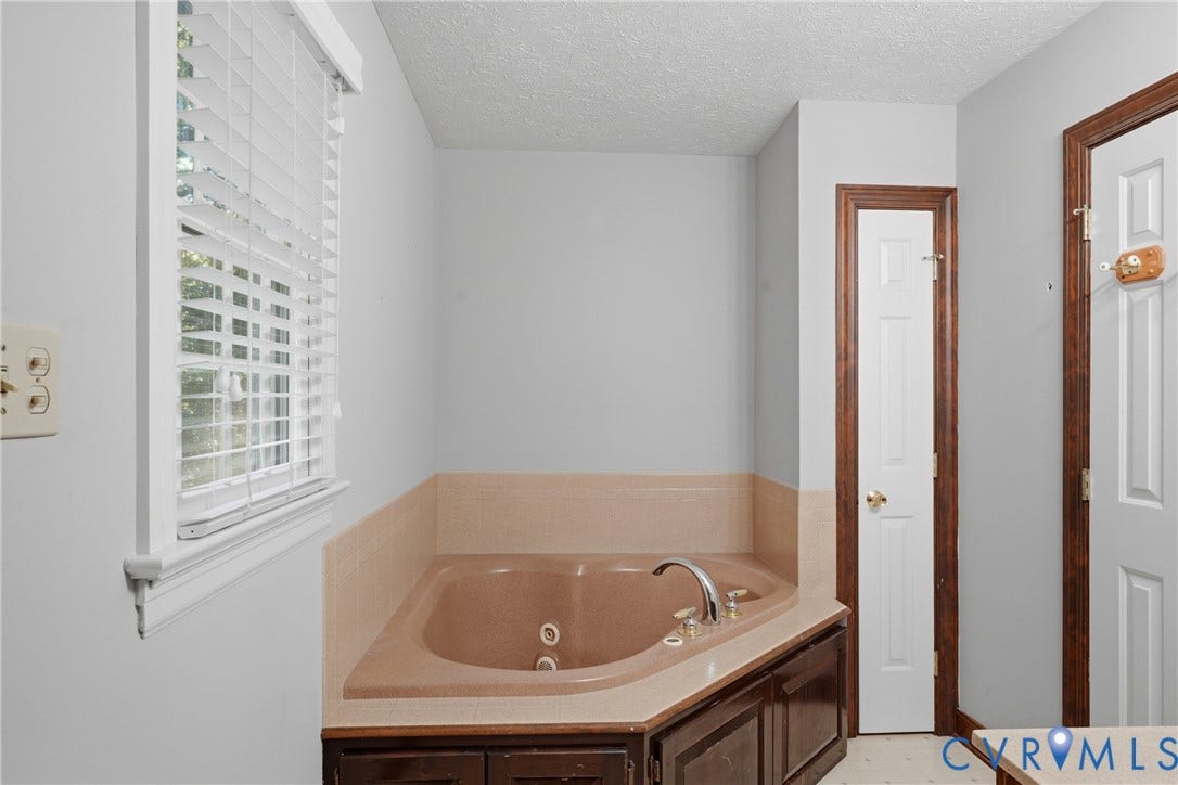 7270 Crossing Oaks Trail, Mechanicsville, VA 23111 Corner jetted tub featuring a tile surround, dark wood-finish cabinetry, metal faucet fixtures, and horizontal slat window blinds