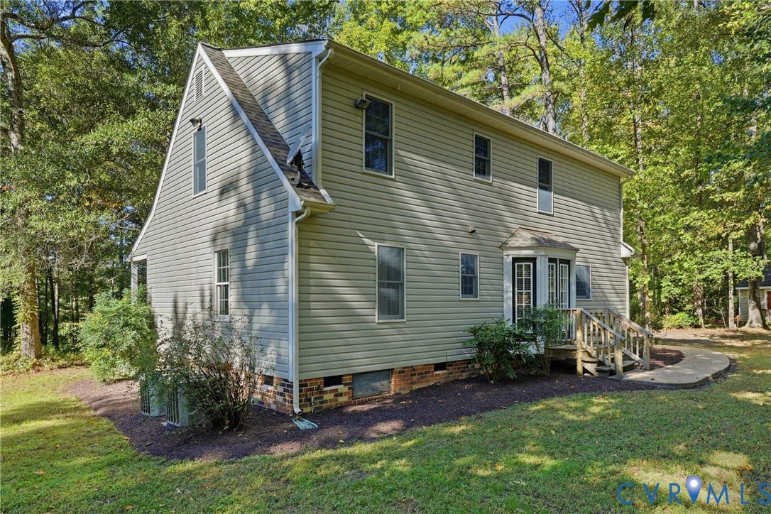 7270 Crossing Oaks Trail, Mechanicsville, VA 23111 Two-story home with vinyl siding, gambrel roofline, raised rear deck, and masonry foundation base, situated on a wooded lot