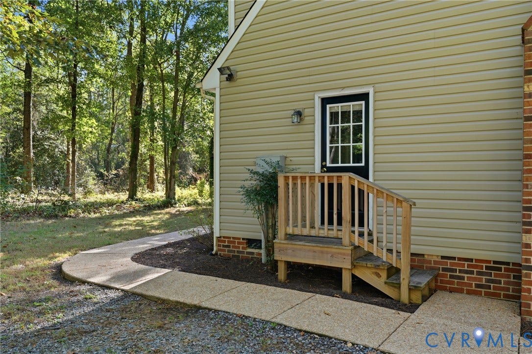 7270 Crossing Oaks Trail, Mechanicsville, VA 23111 Exterior side entry with wood steps and railing, light-colored horizontal siding, brick foundation detail, and paved concrete walkway