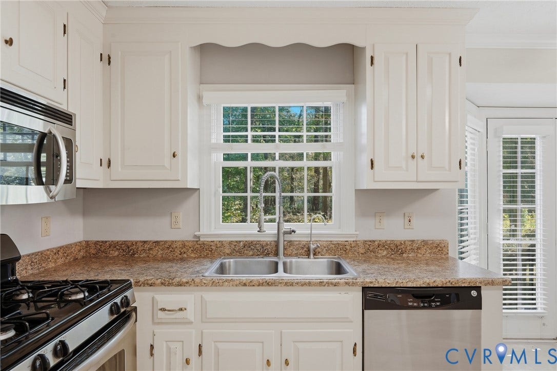 7270 Crossing Oaks Trail, Mechanicsville, VA 23111 White shaker-style cabinetry with overhead scalloped detail, stone-patterned countertops, stainless steel dual-basin sink with arched faucet, and integrated stainless steel appliances