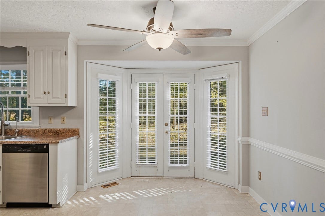 7270 Crossing Oaks Trail, Mechanicsville, VA 23111 Dual French doors with pane glass panels, bay configuration, ceiling fan with integrated lighting, neutral wall palette, and built-in white cabinetry with stone-finish countertops