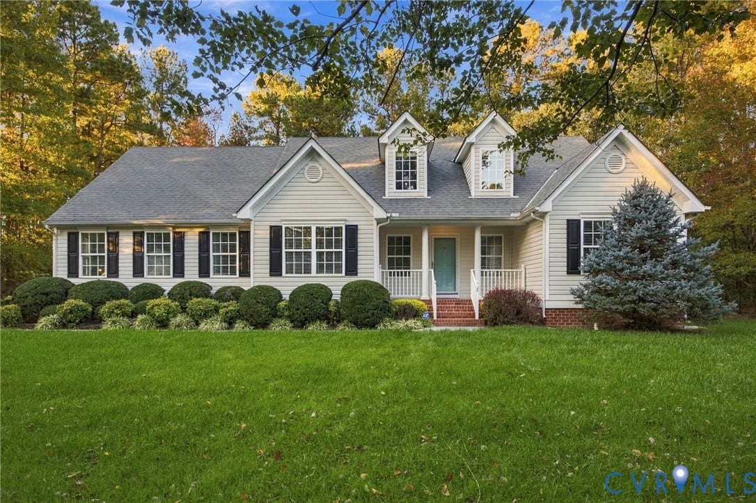 Traditional exterior featuring light-toned lap siding, multiple roof gables, dormer windows, a covered front porch, and brick foundation detailing