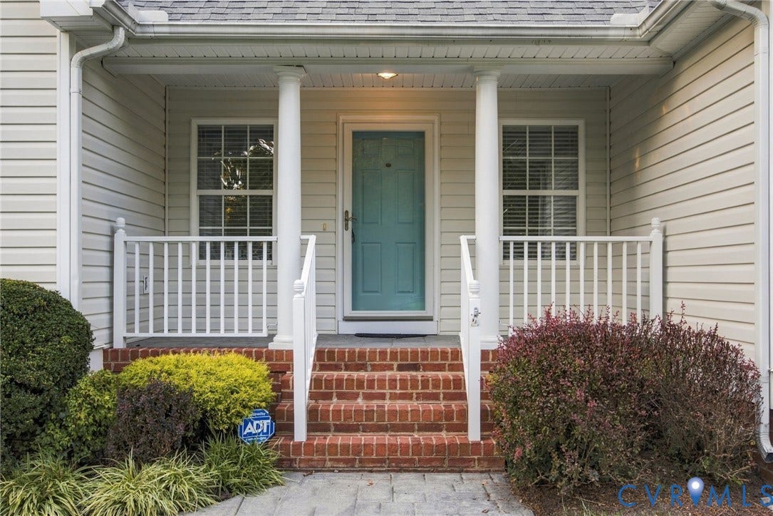 Covered front porch featuring a brick staircase, white spindle railing, twin structural columns, and lap siding exterior