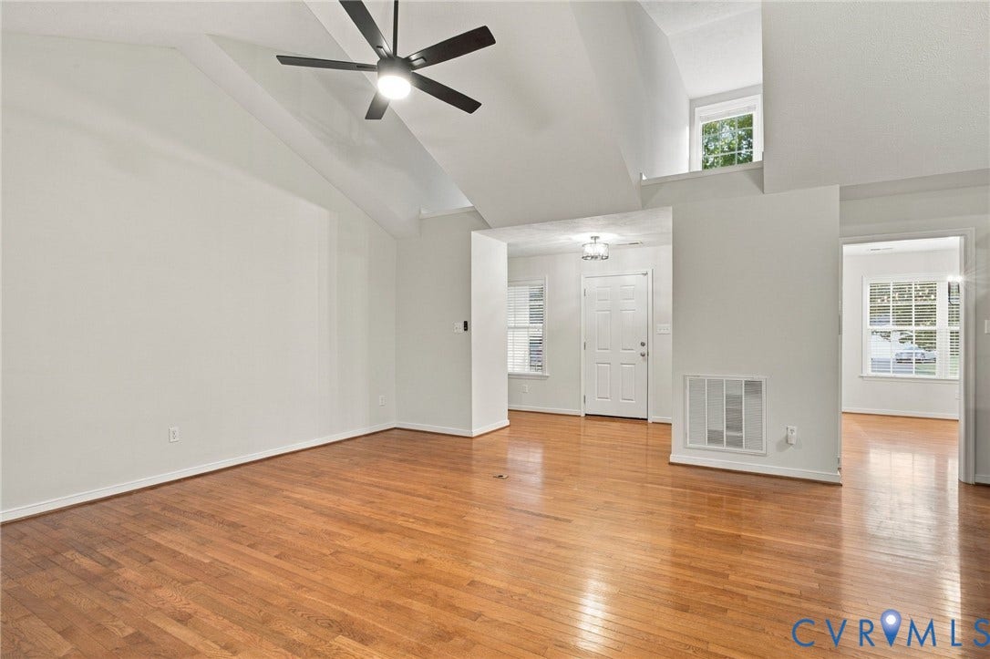 Vaulted ceiling featuring a central lighted ceiling fan, wood-finish flooring, and multiple window placements