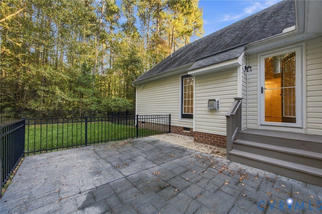 Rear exterior featuring a stamped concrete patio, black metal fencing, brick foundation accents, and a staircase leading to a glass-paneled door
