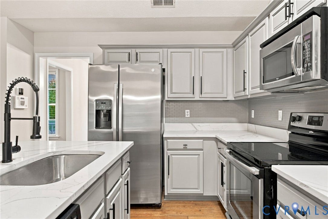 Kitchen featuring white shaker-style cabinetry, stainless steel appliances, white stone-finish countertops, subway tile backsplash, and a matte black gooseneck faucet