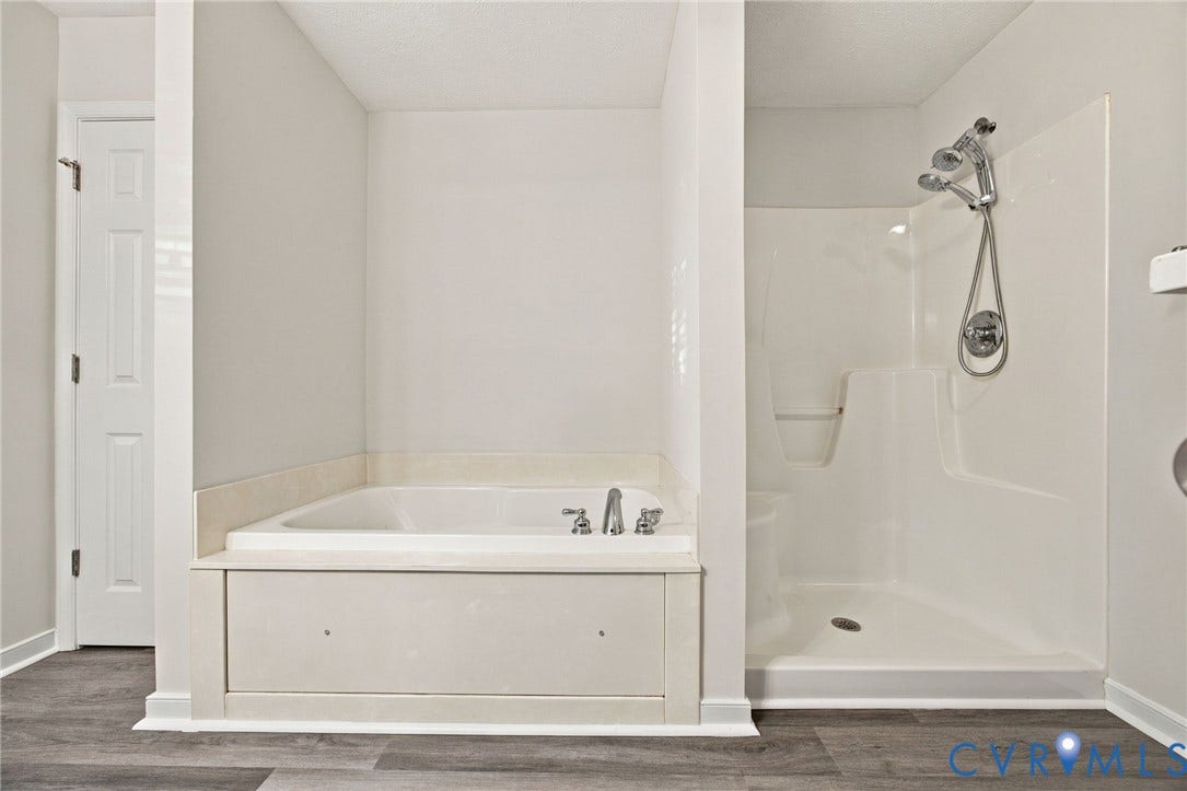 Soaking tub with a tile surround, separate stall shower with molded acrylic surround, adjustable handheld shower fixture, and wood-finish flooring
