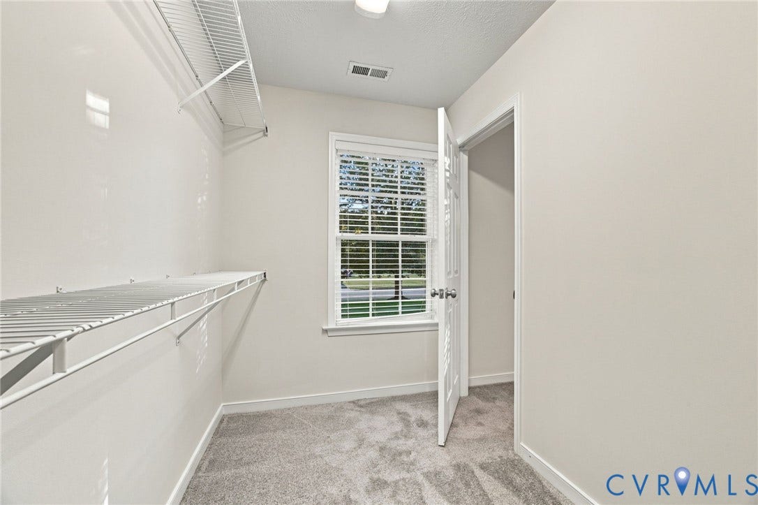 Storage area featuring wall-mounted wire shelving, a window with horizontal blinds, neutral carpeting, and a traditional hinged door