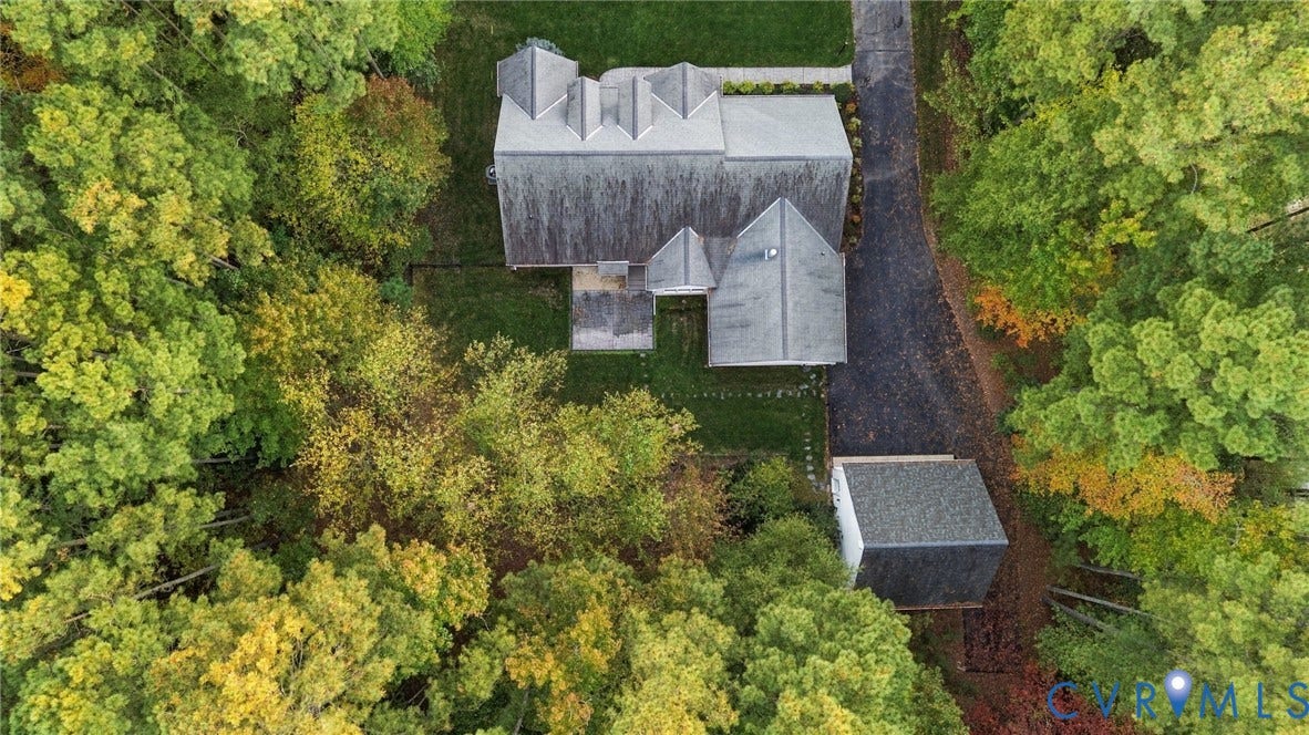 Aerial perspective of a detached residence featuring a multi-gabled roofline, a paved driveway, and a detached structure, all situated on a wooded lot with mature trees