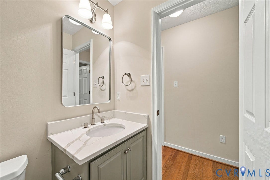 Vanity featuring a stone-look countertop with an integrated oval sink, chrome faucet hardware, cabinetry with recessed panel doors, and a rectangular wall-mounted mirror