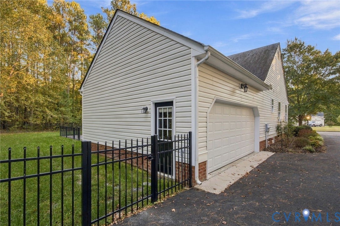 Exterior side elevation featuring vinyl siding, a multi-car garage, brick foundation detailing, and black metal perimeter fencing