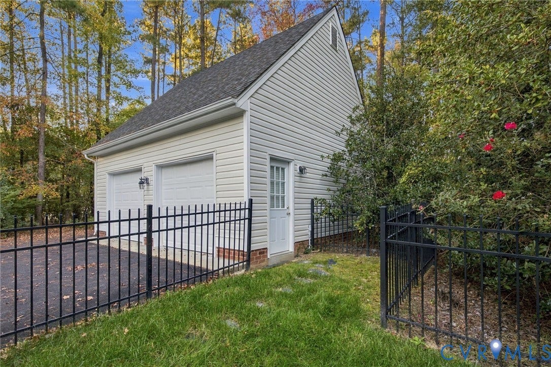 Detached two-car garage featuring light-colored horizontal siding, asphalt shingle roofing, brick foundation accents, and metal perimeter fencing