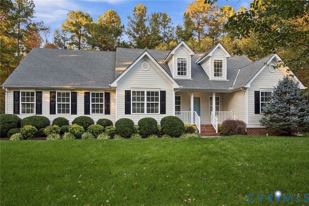 Vinyl-sided exterior featuring double-hung windows, decorative shutters, a gabled roofline with dual dormers, and a covered front porch with brick steps