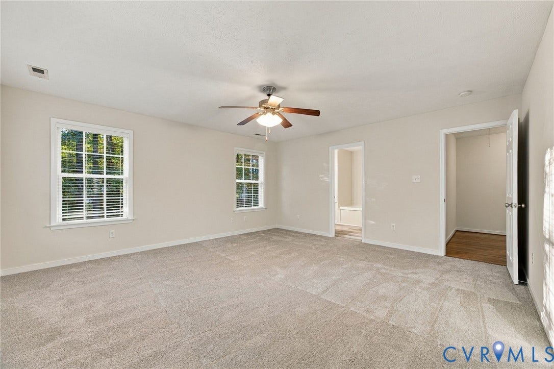 Spacious interior featuring neutral wall-to-wall carpeting, multiple windows with grid detailing, and a ceiling-mounted light fixture with a fan