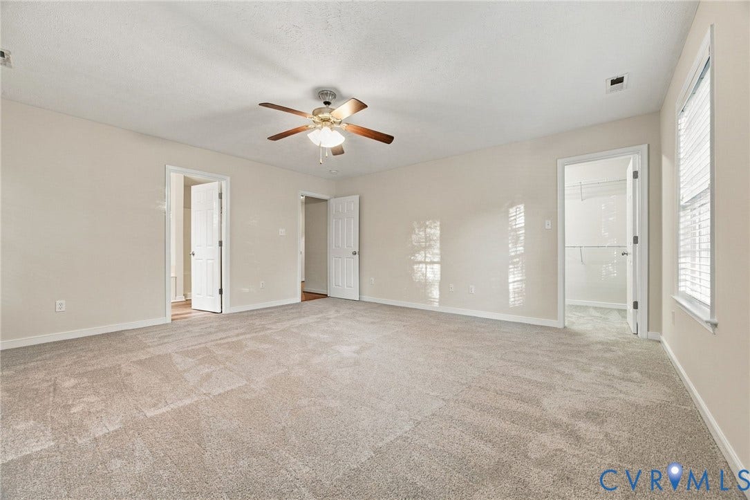 Spacious room featuring neutral wall tones, wall-to-wall carpeting, a ceiling fan with integrated lighting, and a walk-in closet with built-in shelving