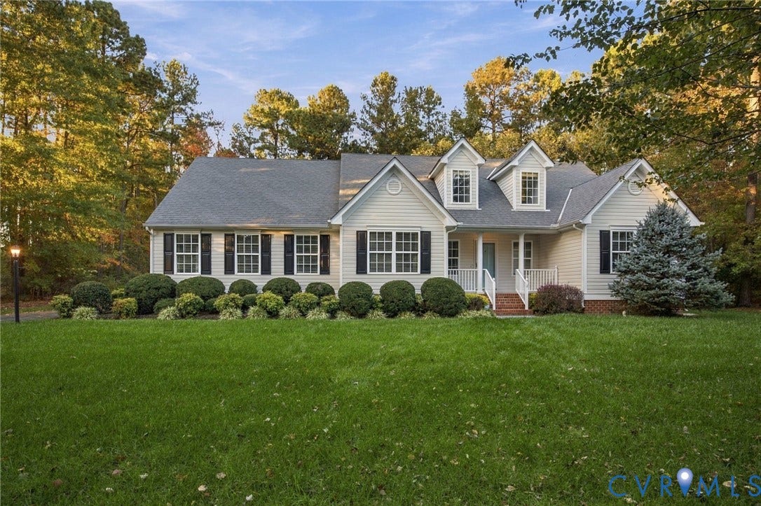 Two-story residence featuring light-toned horizontal siding, dark decorative shutters, dual gabled dormers, a covered front porch with a brick staircase, and a large front lawn