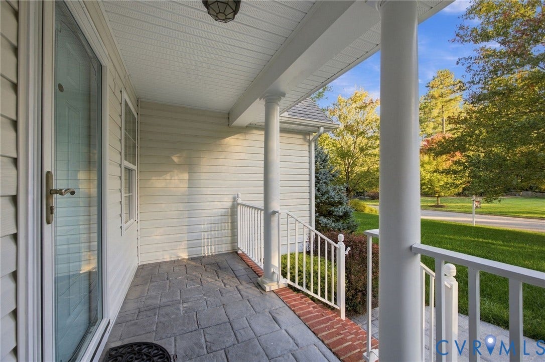 Covered front porch featuring stamped concrete flooring, white column supports, white metal railing, and brick border detailing