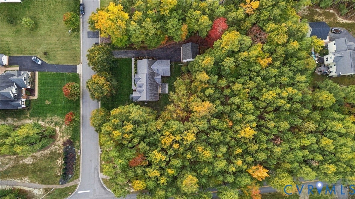 Aerial perspective of a residential property featuring a paved driveway, detached storage structure, multi-pitch roofline, and expansive wooded grounds
