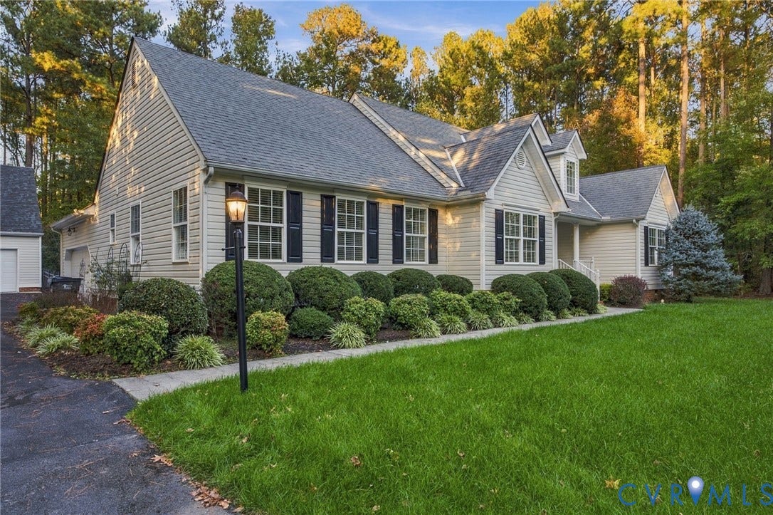 Traditional siding exterior featuring a gable roofline, multi-pane windows with dark shutters, and mature professional landscaping