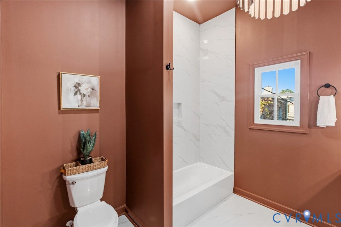3104 E Broad Street, Richmond, VA 23223 Bathroom featuring a tub-shower combination with full-height stone-finish wall tile, a recessed wall niche, a multi-pane window, and a circular wall-mounted towel ring