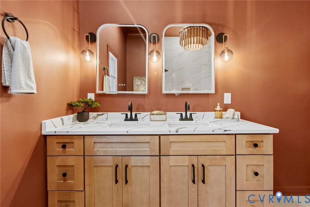 3104 E Broad Street, Richmond, VA 23223 Double vanity featuring a white countertop with grey veining, light wood-finish cabinetry, two arched mirrors, matte black fixtures, and dual wall-mounted pendant lights