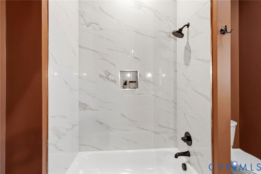 3104 E Broad Street, Richmond, VA 23223 Shower enclosure featuring white stone-finish wall tile with grey veining, a built-in recessed niche, and matte black plumbing fixtures