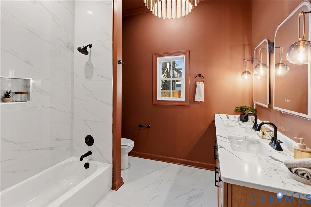 3104 E Broad Street, Richmond, VA 23223 Bathroom featuring a dual-sink vanity with a stone-finish countertop, matte black fixtures, arched vanity mirrors, a tiled shower surround, and a drum-style pendant light