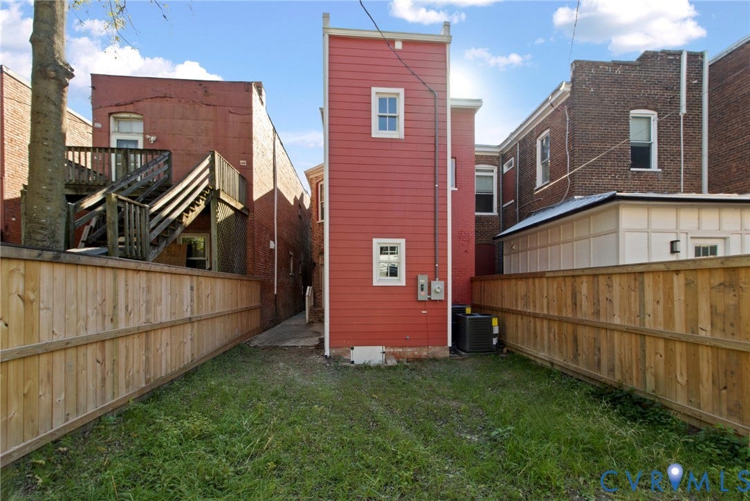 3104 E Broad Street, Richmond, VA 23223 Rear exterior featuring horizontal red siding, double-hung windows, and a wood privacy fence enclosing the yard area